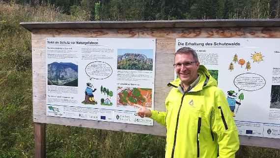 Schutzwaldexperte Starsich von der Wildbach- und Lawinenverbauung vor einer Schautafel zum Thema "Wald als Schutz vor Naturgefahren".